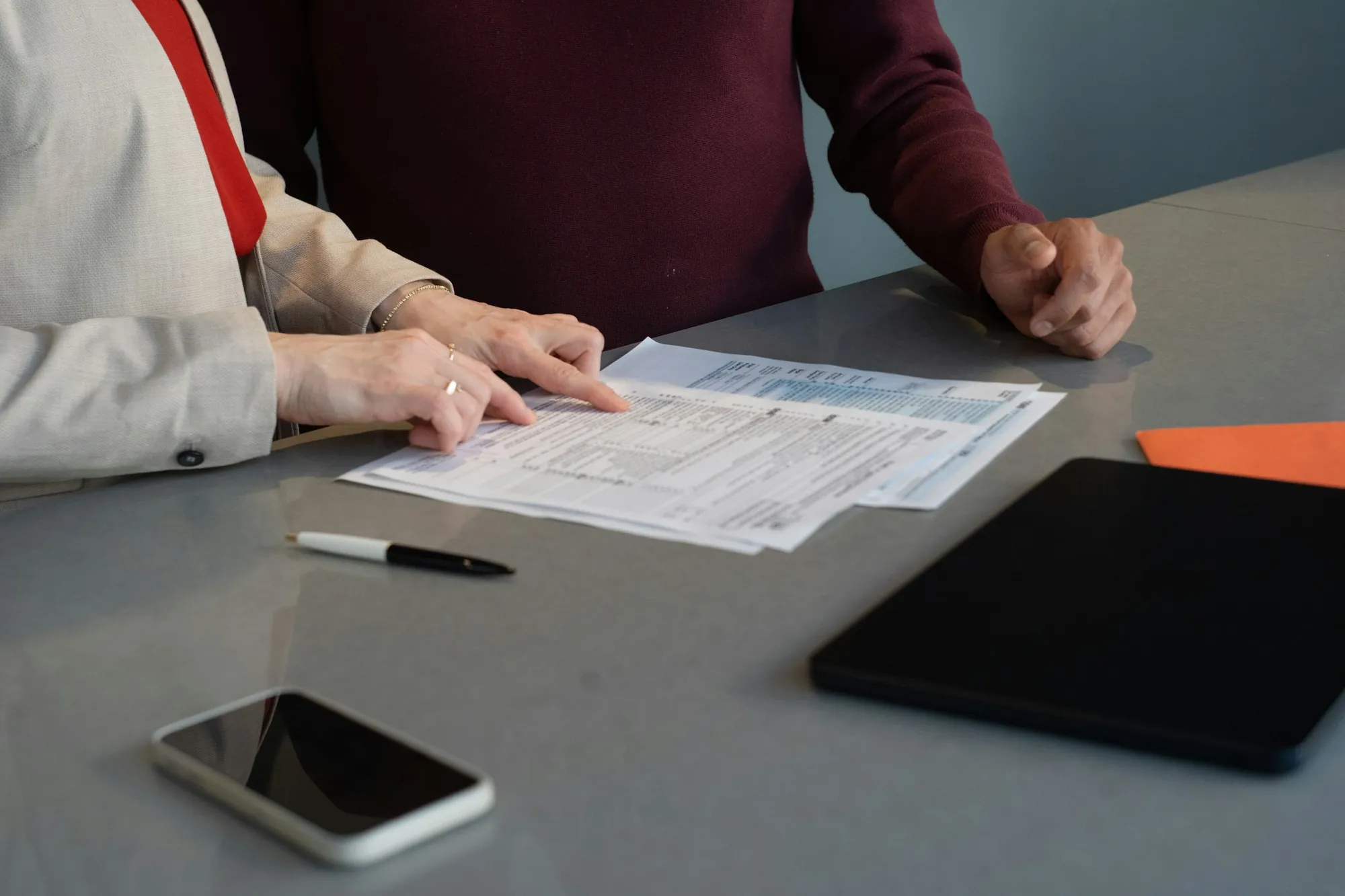 People reviewing printed paperwork at a gray table