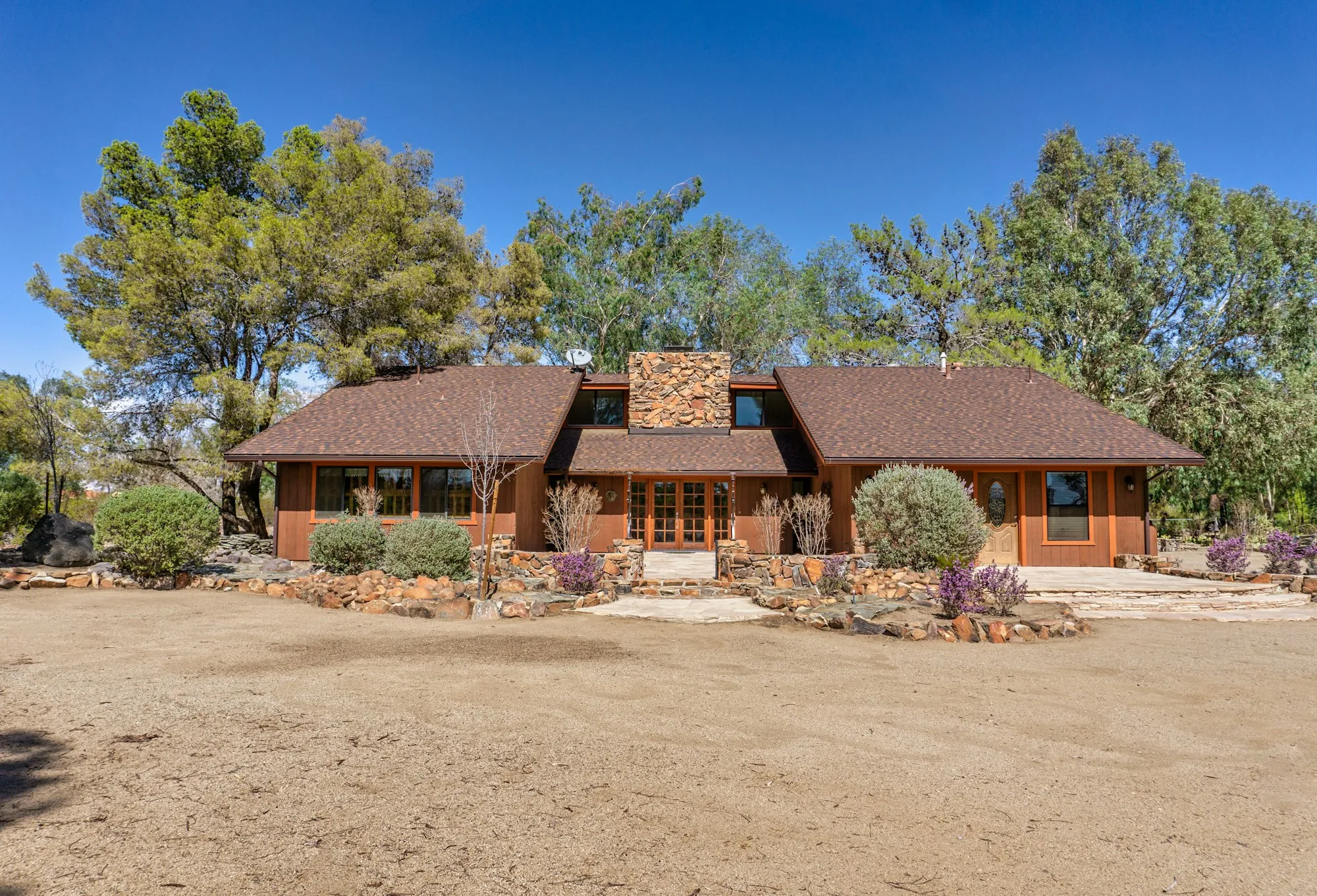 Ranch house with a stone chimney set among trees on a dry lot